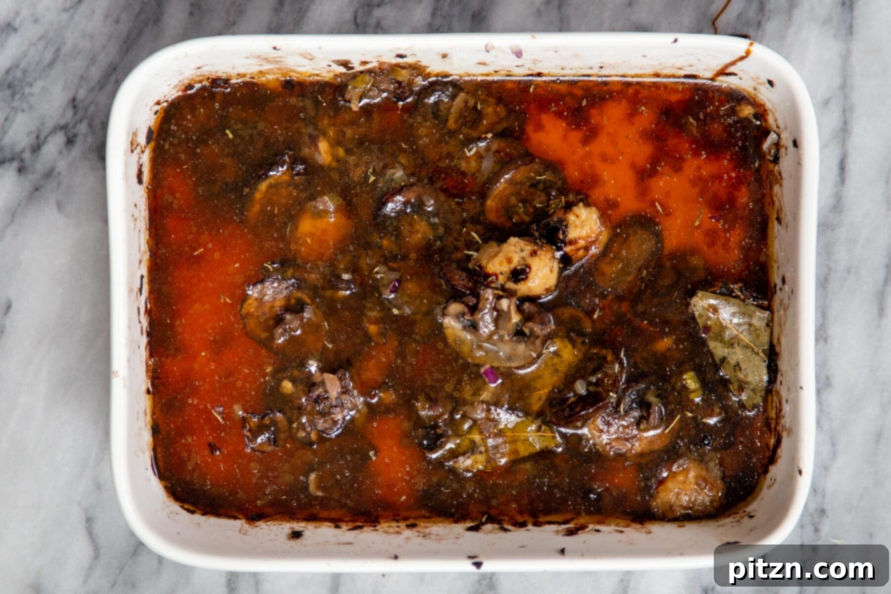 Sliced baked mushrooms and savory broth combined in a casserole dish, ready for the addition of rice.