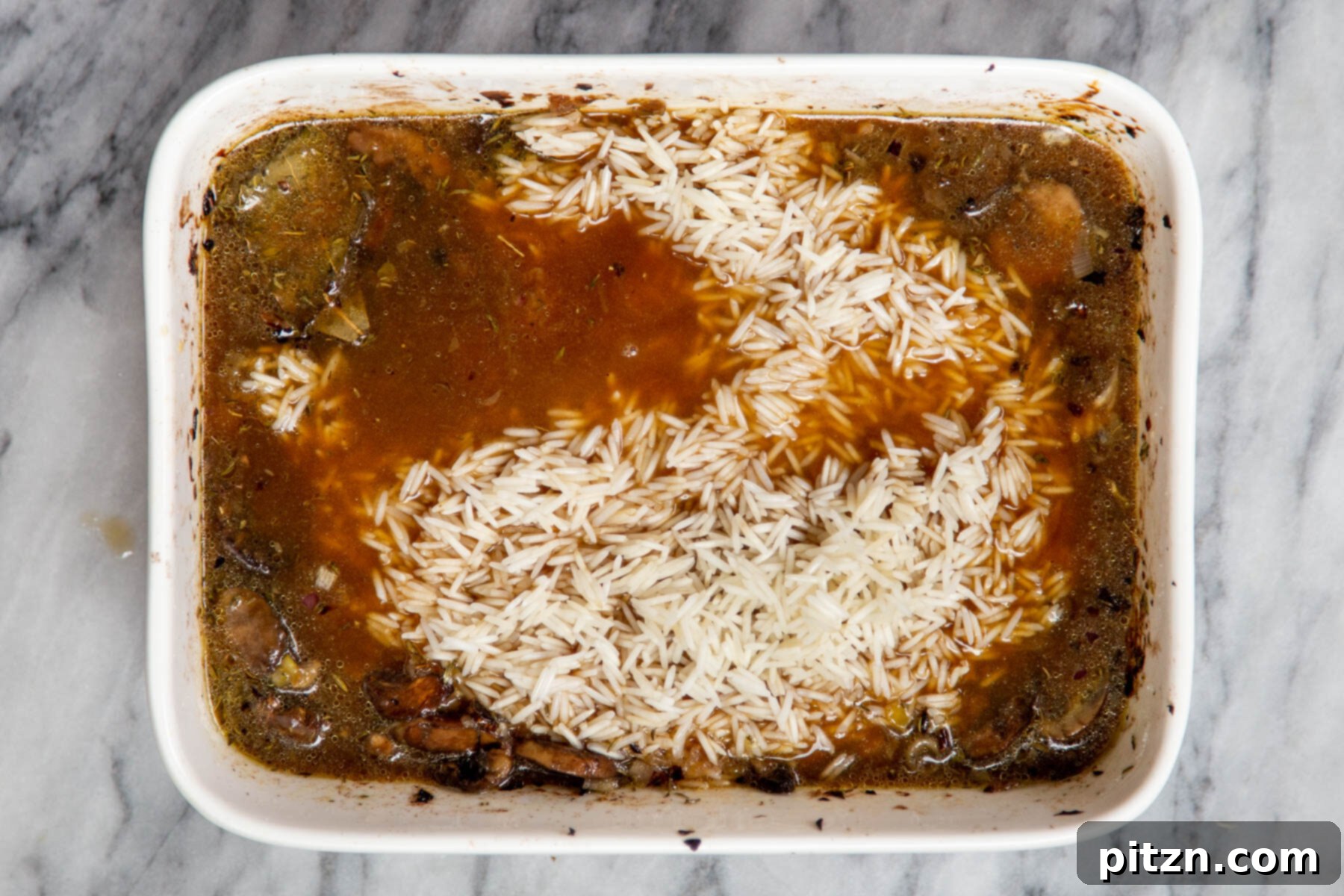 Uncooked basmati rice, mushrooms, and broth combined in a white casserole dish, stirred and ready for baking.