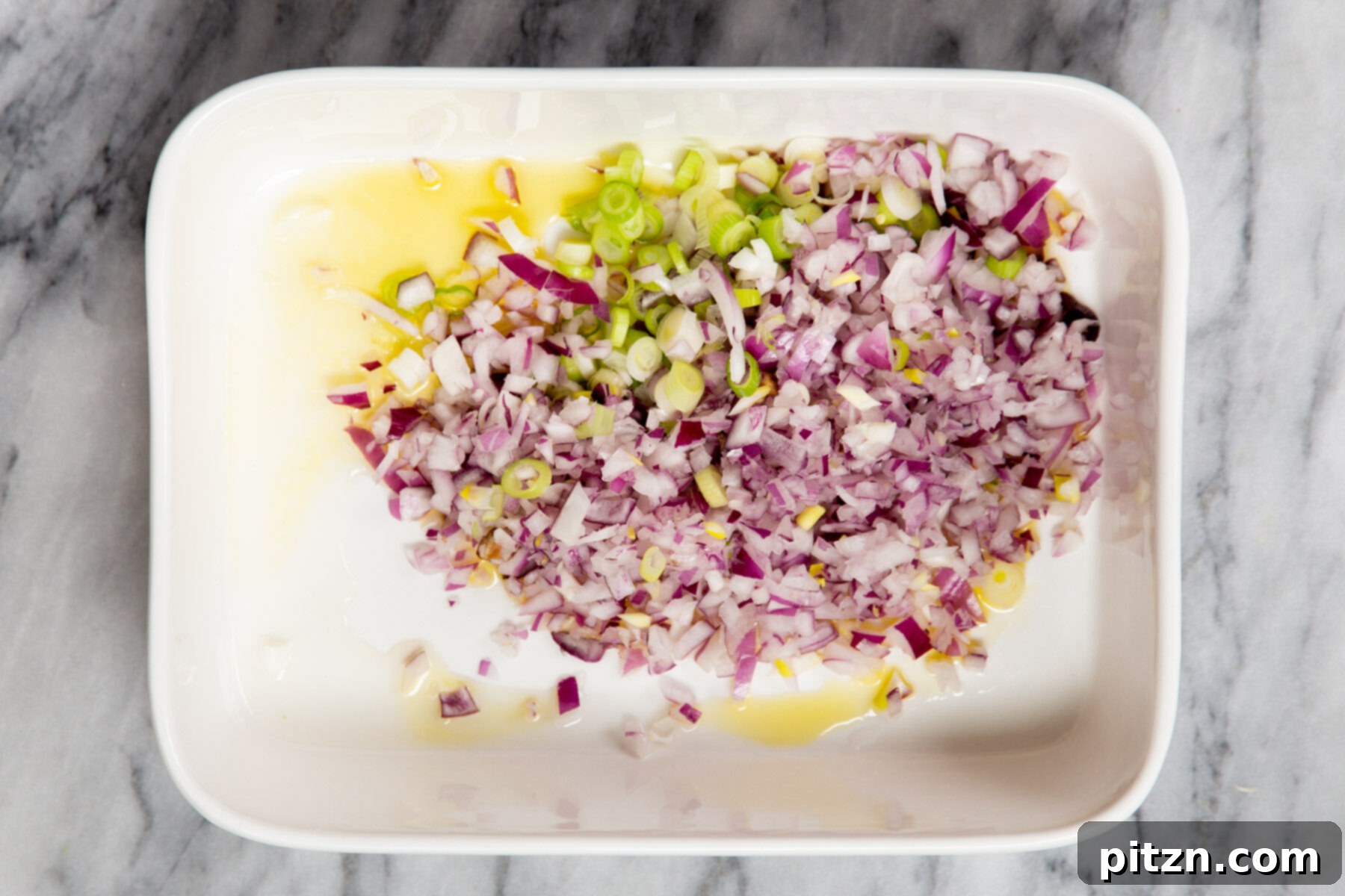 Minced onion, garlic, and green onion in a casserole dish, seasoned and ready for the next step of the baked mushroom rice recipe.