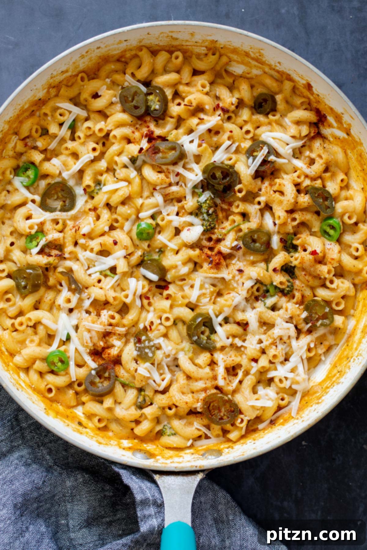 Fiery Vegan Skillet Mac and Cheese 3 An overhead view of a hot skillet filled with creamy vegan jalapeño mac and cheese, garnished with additional jalapeño slices and a sprinkle of vegan cheese shreds.