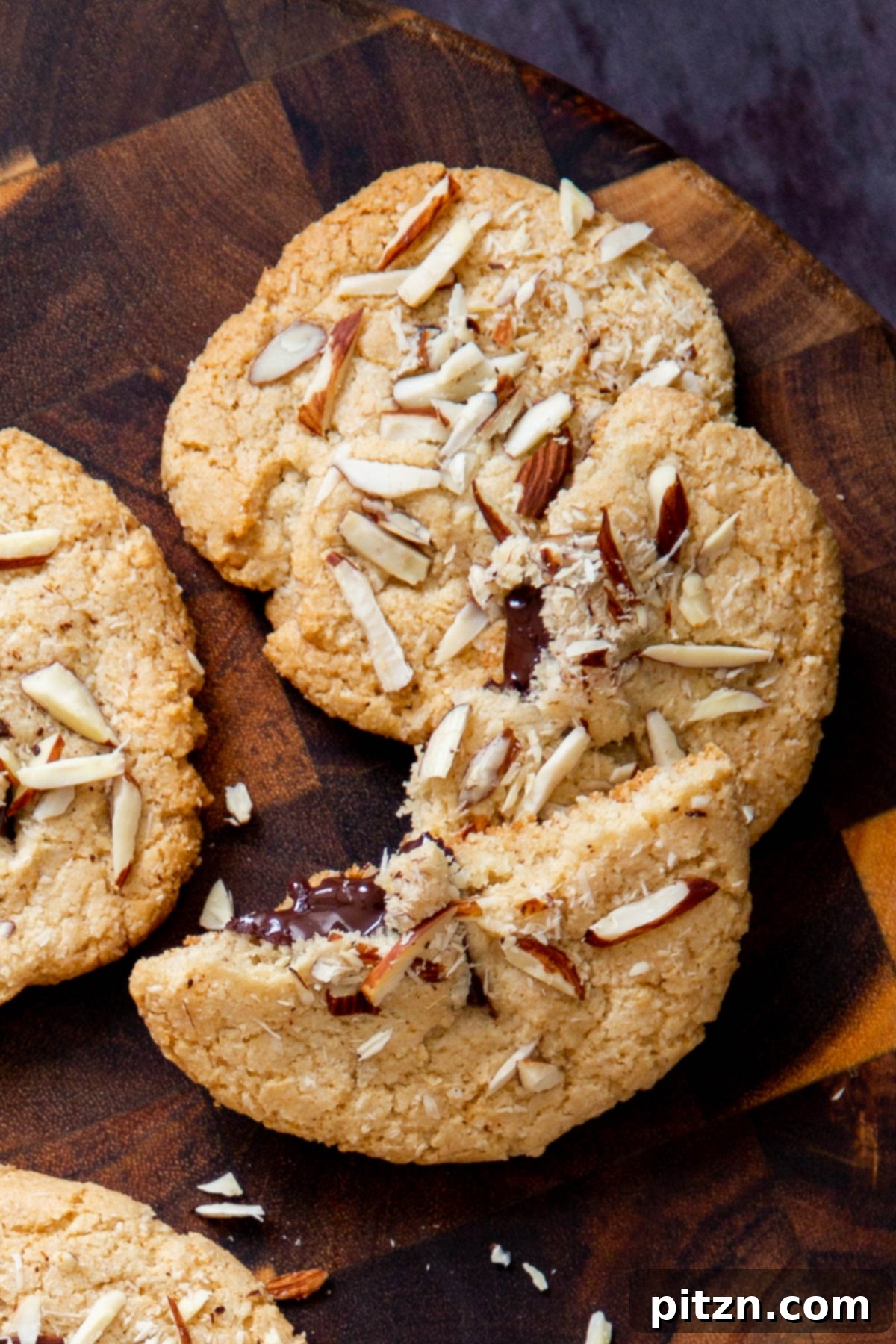 Irresistible Vegan Gluten-Free Almond Coconut Joy Cookies 3 Halved vegan Almond Joy cookies showing melted chocolate chunks on a wooden board, showcasing their decadent center