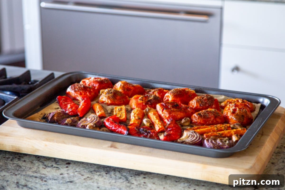 Velvet Roasted Tomato Bliss 10 Beautifully roasted bell peppers, tomatoes, garlic, and onions, caramelized and tender, spread on a baking sheet after oven cooking.