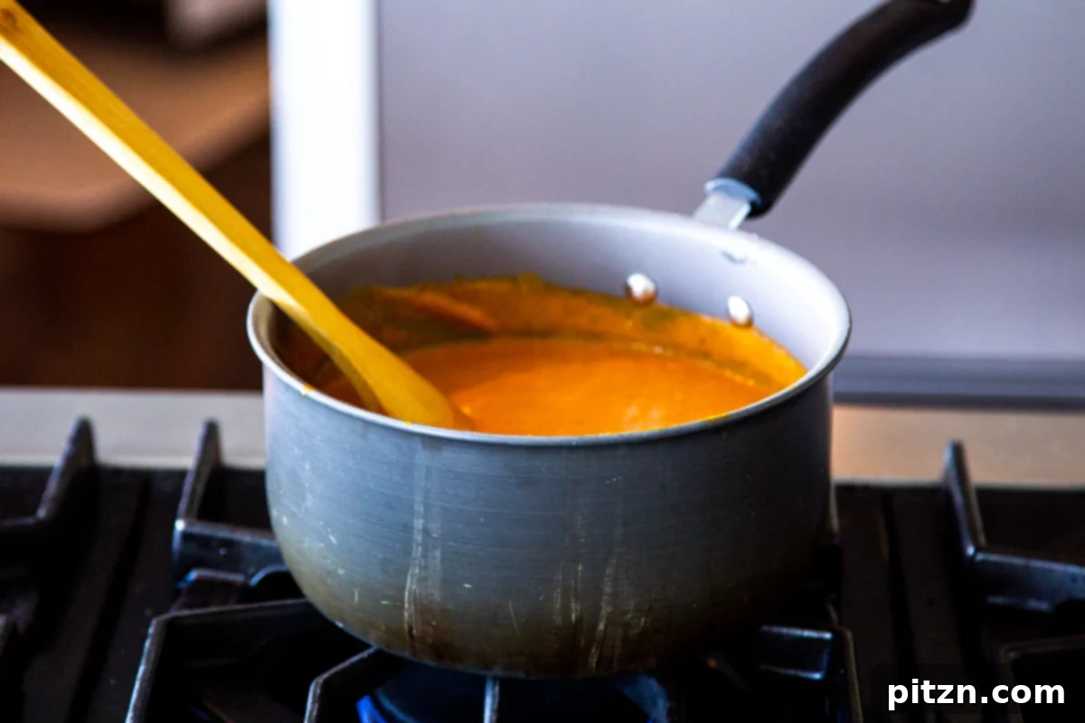 Velvet Roasted Tomato Bliss 13 A pot of rich, red roasted tomato soup simmering gently on a gas stove, filling the kitchen with its inviting aroma.