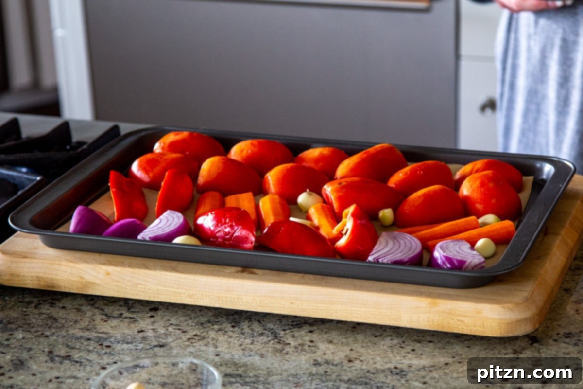 Velvet Roasted Tomato Bliss 8 Assortment of fresh vegetables, including tomatoes, bell peppers, carrots, and onions, neatly arranged on a baking sheet, ready for seasoning.