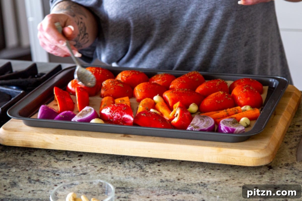 Velvet Roasted Tomato Bliss 9 Fresh bell peppers, tomatoes, and onion slices on a baking sheet being generously drizzled with a fragrant seasoned olive oil.