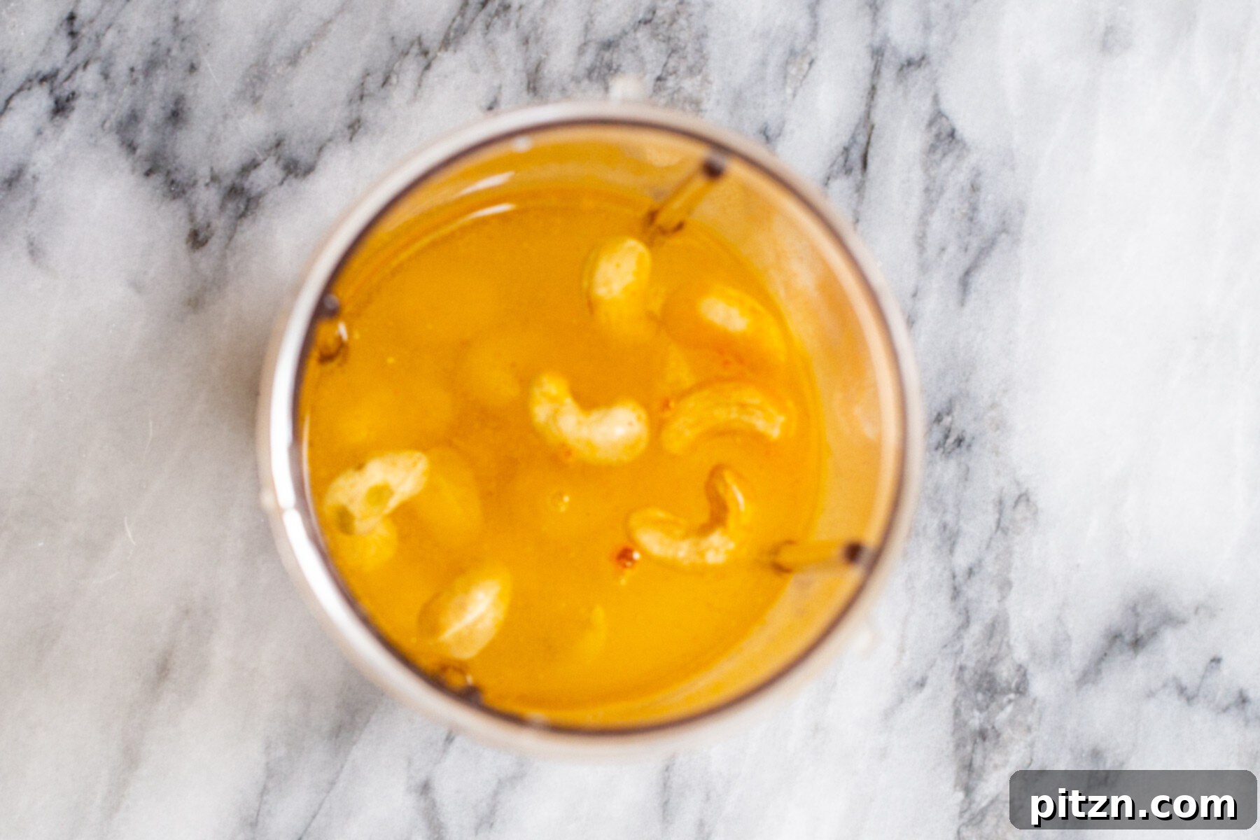 Plant-Based Boston Dream Cake 15 Raw cashews, turmeric, and water in a blender, showing the initial stages of making the vibrant yellow vegan vanilla custard.