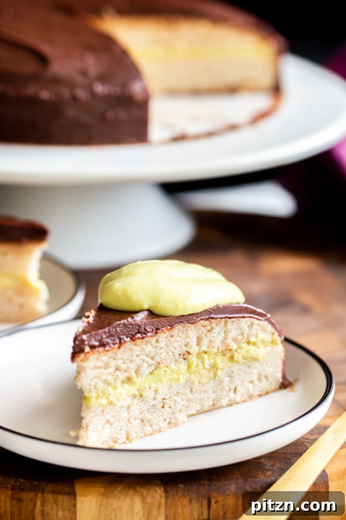 Plant-Based Boston Dream Cake 3 A close-up view of a slice of vegan Boston Cream Pie, showcasing the thick layer of homemade vegan vanilla custard between the sponge cake layers.