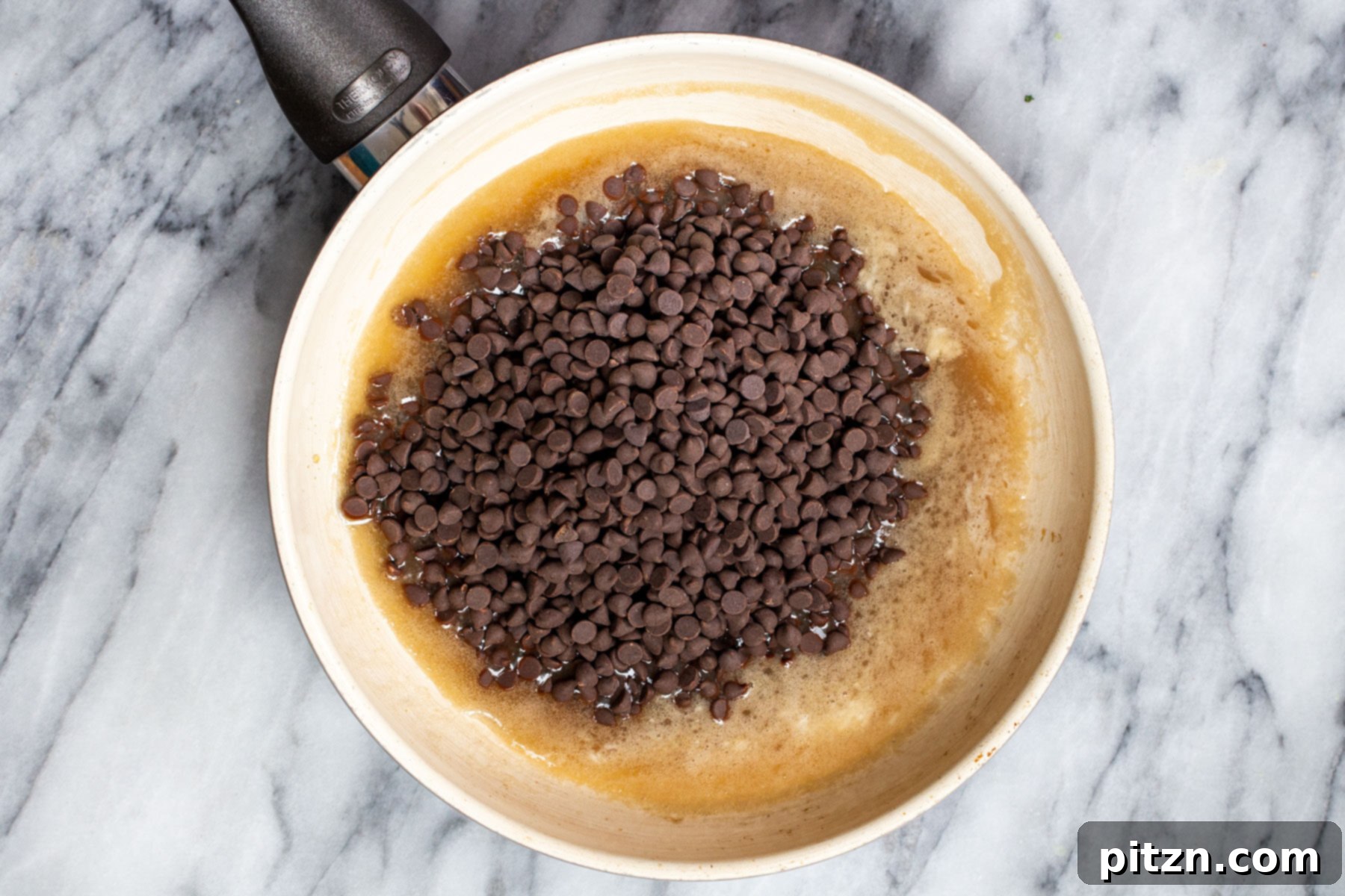 Plant-Based Boston Dream Cake 22 Vegan chocolate chips melting into the hot coconut cream and maple syrup mixture in a sauté pan, beginning to form the ganache.