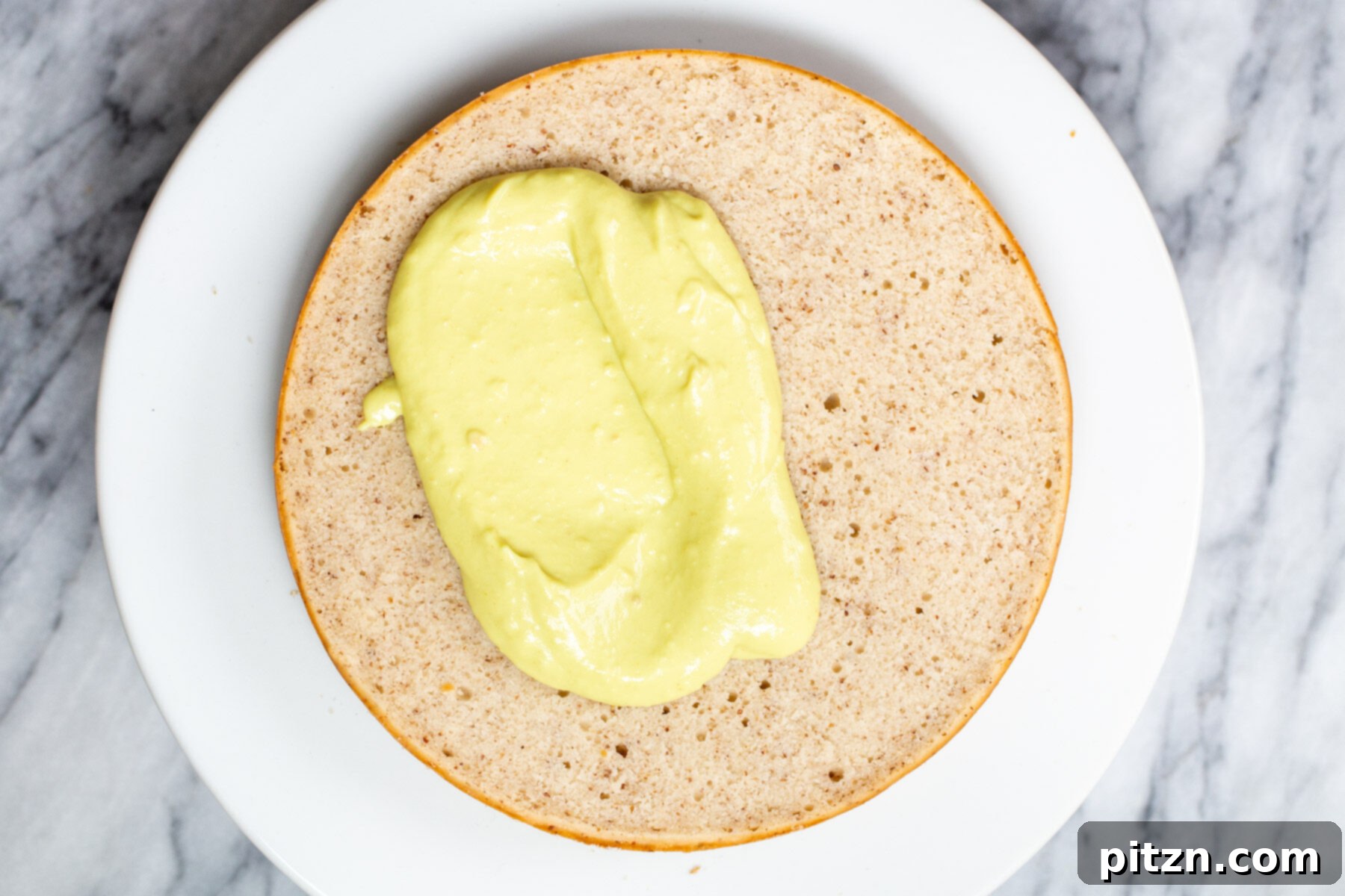 Plant-Based Boston Dream Cake 25 Vegan vanilla custard being meticulously spread onto one layer of the sliced sponge cake with an offset spatula, creating an even filling.