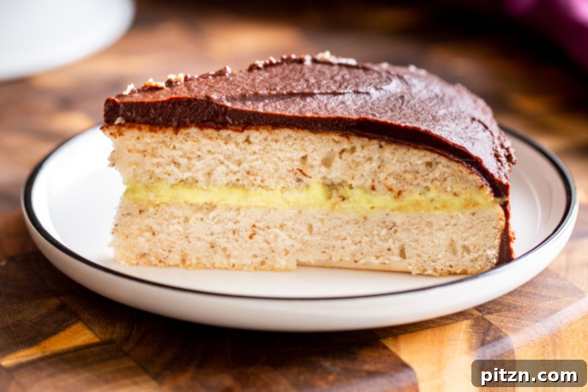Plant-Based Boston Dream Cake 29 A beautiful slice of Vegan Boston Cream Pie Cake resting on a rustic wooden board, showcasing its distinct layers of cake, custard, and chocolate ganache.
