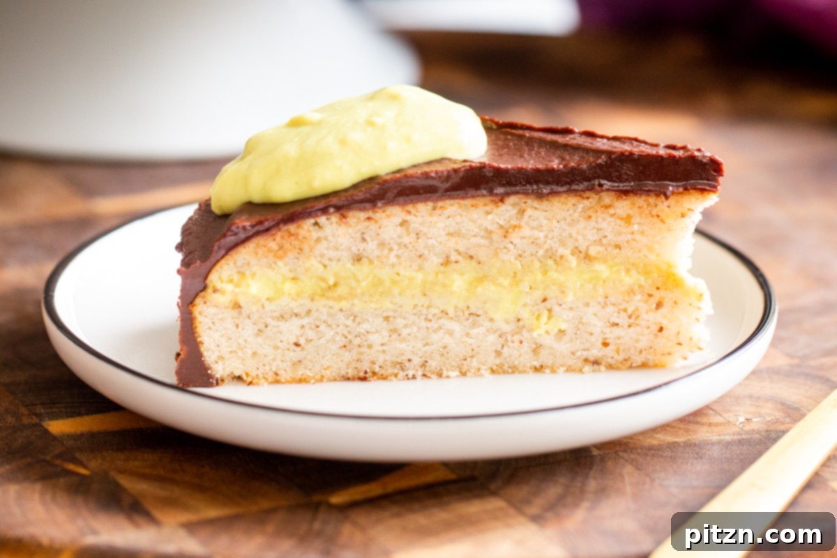 Plant-Based Boston Dream Cake 30 A beautiful side profile of a slice of vegan Boston Cream Pie Cake, highlighting the distinct layers of fluffy cake, creamy custard, and glossy chocolate ganache on a wooden board.