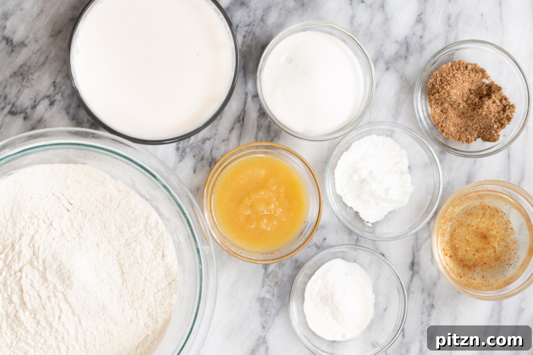 Plant-Based Boston Dream Cake 5 A collection of ingredients laid out on a marble countertop, including non-dairy milk, oil, sugar, flour, and extracts, ready for making vegan sponge cake.