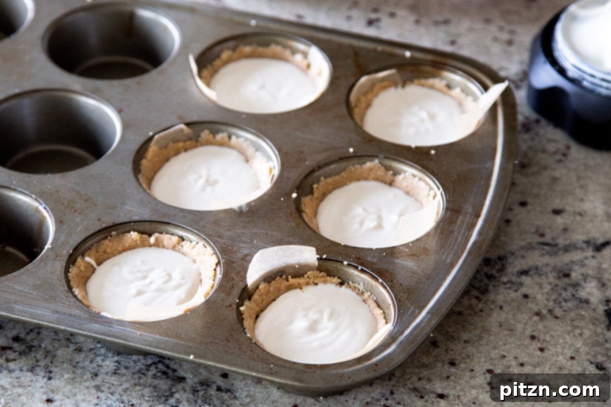 Mini Apple Pie Cheesecake Delights 12 Mini vegan cheesecakes nestled in a metal muffin tin, topped with a rich apple filling and ready for baking