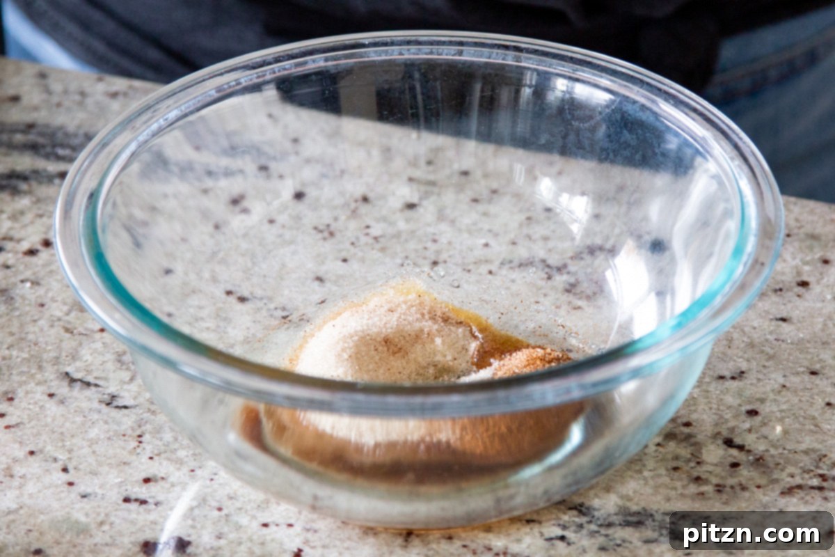 Mini Apple Pie Cheesecake Delights 13 A clear glass bowl containing a mix of cinnamon, sugar, and maple syrup for the apple topping
