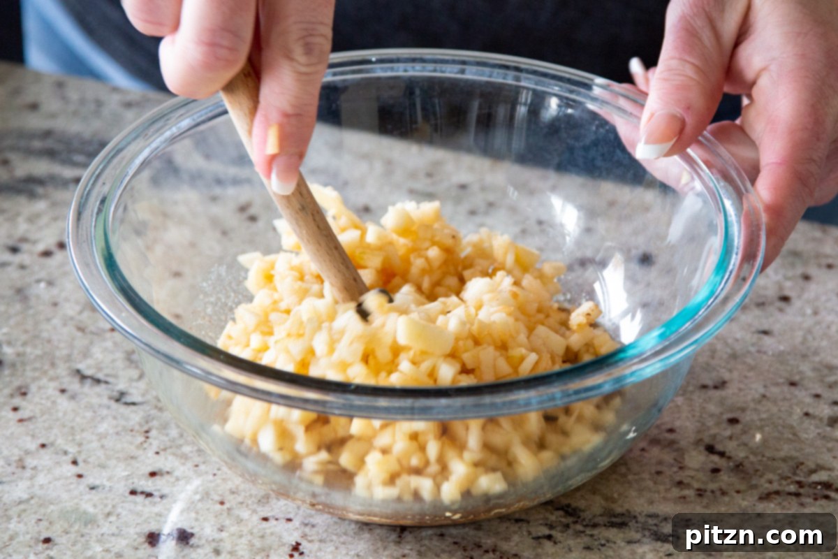 Mini Apple Pie Cheesecake Delights 14 Finely chopped apple chunks being tossed with maple syrup, cinnamon, and sugar in a glass bowl, creating the apple pie topping