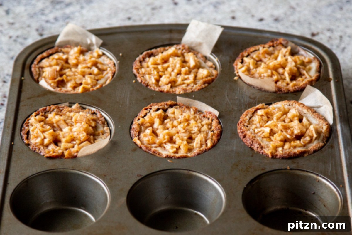Mini Apple Pie Cheesecake Delights 16 Freshly baked vegan apple mini cheesecakes cooling down in a muffin tin, their golden tops glistening