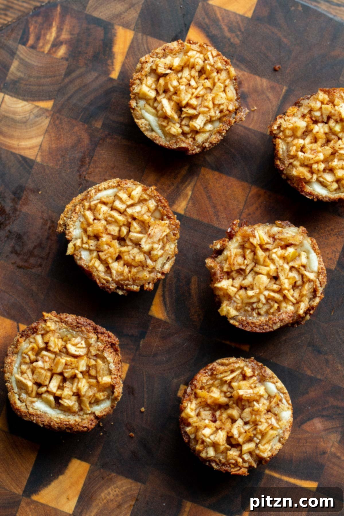 Mini Apple Pie Cheesecake Delights 4 Vegan mini apple cheesecake pies cooling on a wooden board, showcasing their beautiful golden crust and apple topping
