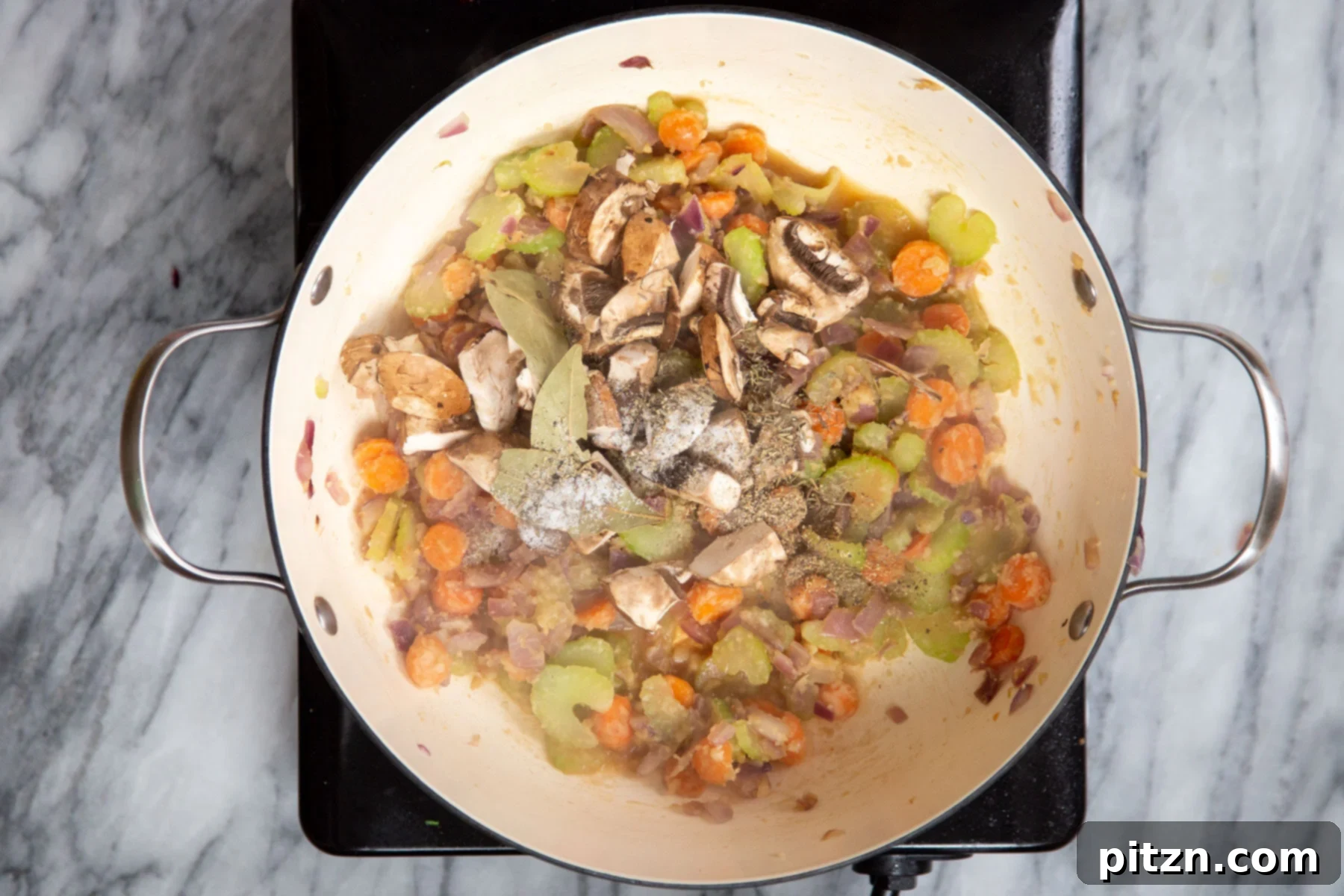 Vegetables and flour mixture frying gently in a deep sauté pan, forming the base of the stew.