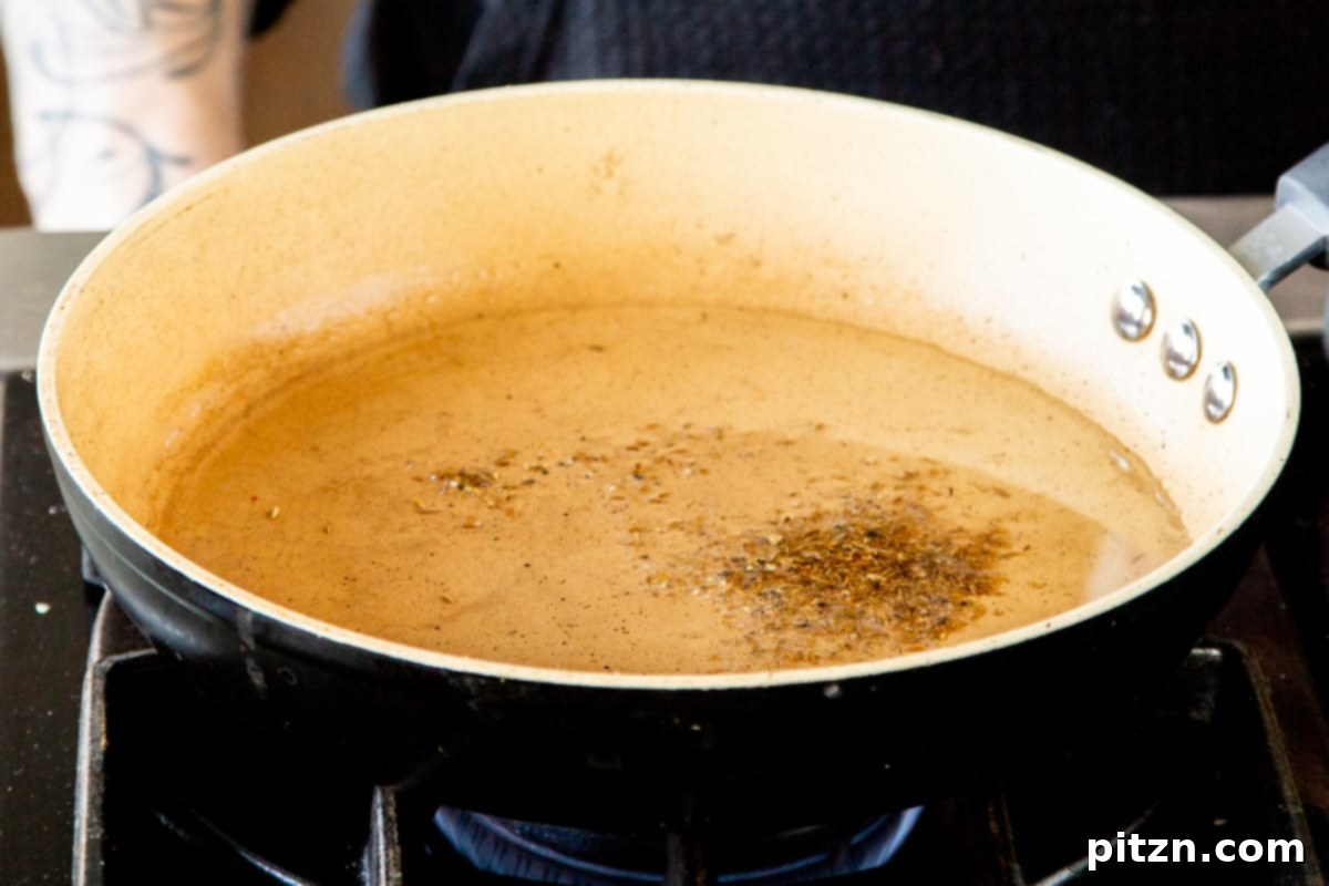 Caramelized Onion Lentil Stew 10 A sizzling frying pan with hot oil, showcasing a scattering of cumin seeds and crushed black peppercorns, releasing their fragrant essence as they temper.