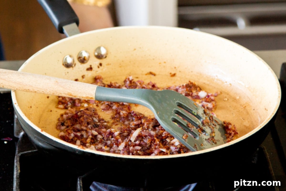 Caramelized Onion Lentil Stew 12 A close-up of finely minced onions, now golden brown and deeply caramelized, sizzling in a sautéing pan, forming the rich flavor base for the dal.