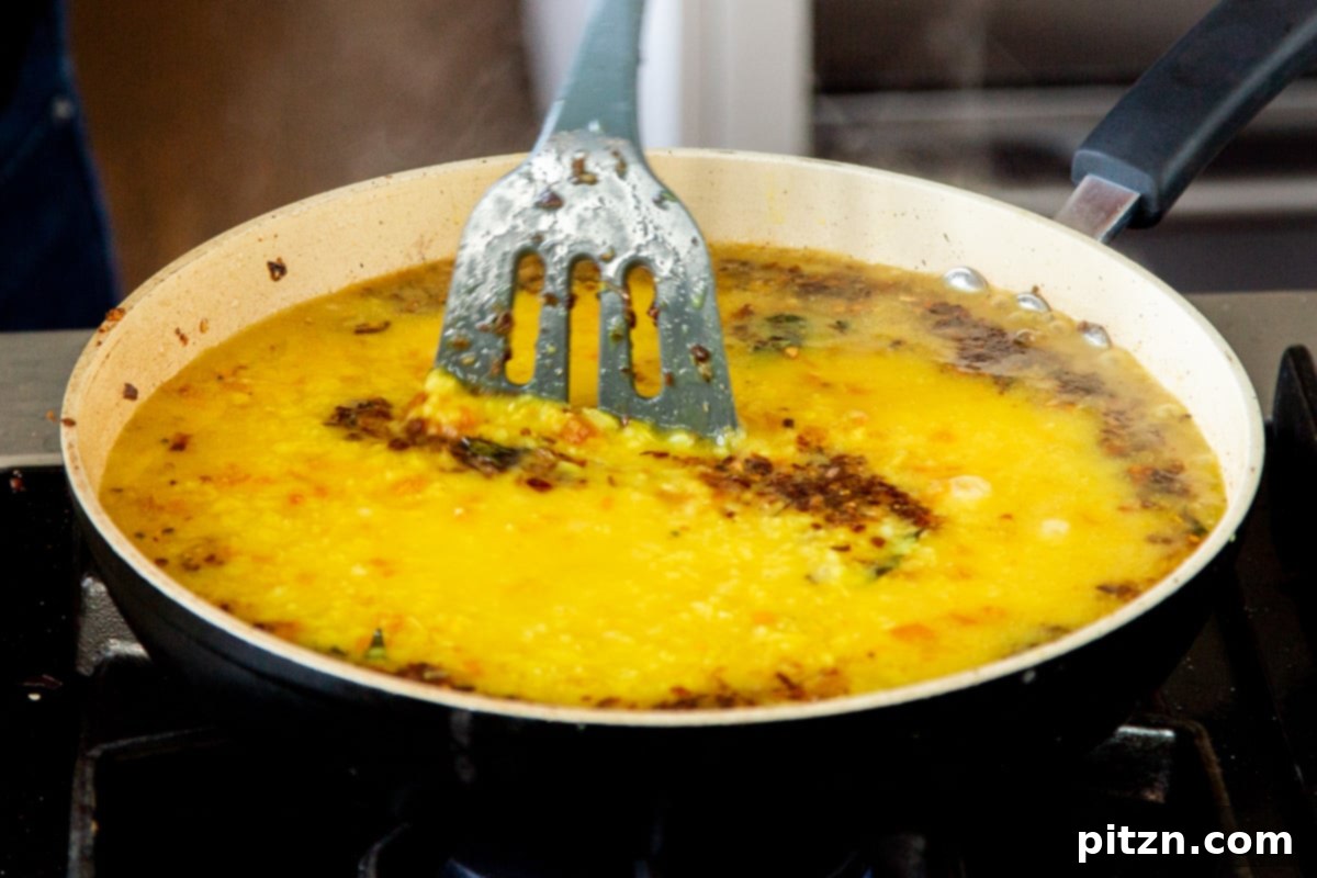 Caramelized Onion Lentil Stew 15 A vibrant tempering of spices and aromatics being carefully poured over a large pot of dal, creating a delicious marriage of flavors and a visually appealing layer.