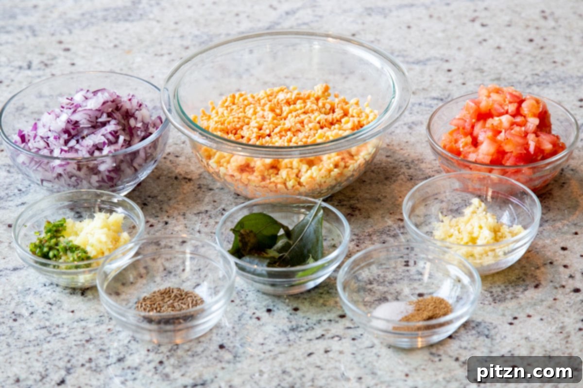 Caramelized Onion Lentil Stew 7 A beautifully arranged collection of fresh ingredients for making caramelized onion dal, including various lentils, a whole tomato, onions, garlic, ginger, and whole spices, all laid out on a clean marble countertop.