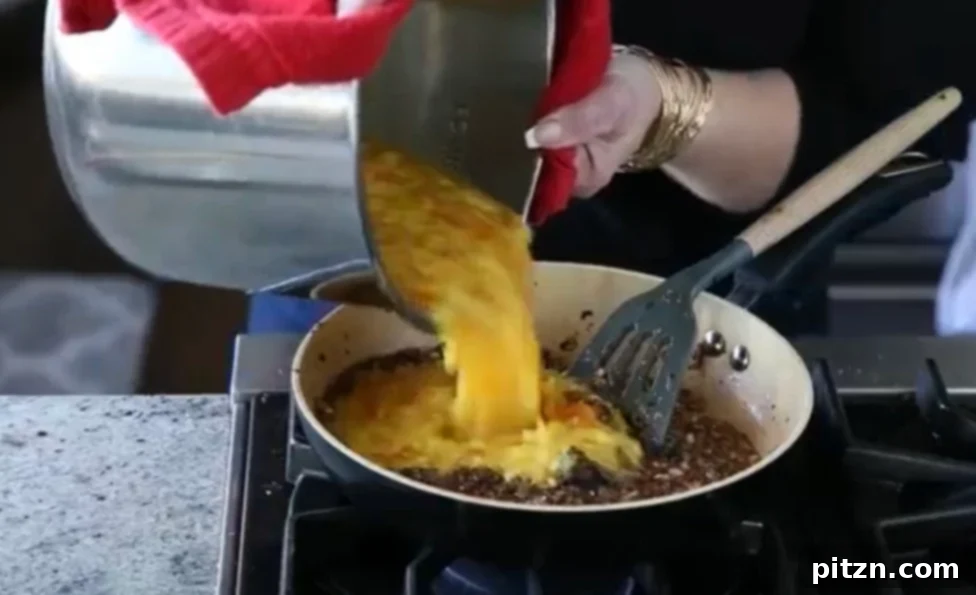 Caramelized Onion Lentil Stew 8 Cooked lentils being carefully poured into a skillet containing a vibrant caramelized onion tadka, signifying the delicious combination of flavors in the making of the dal.