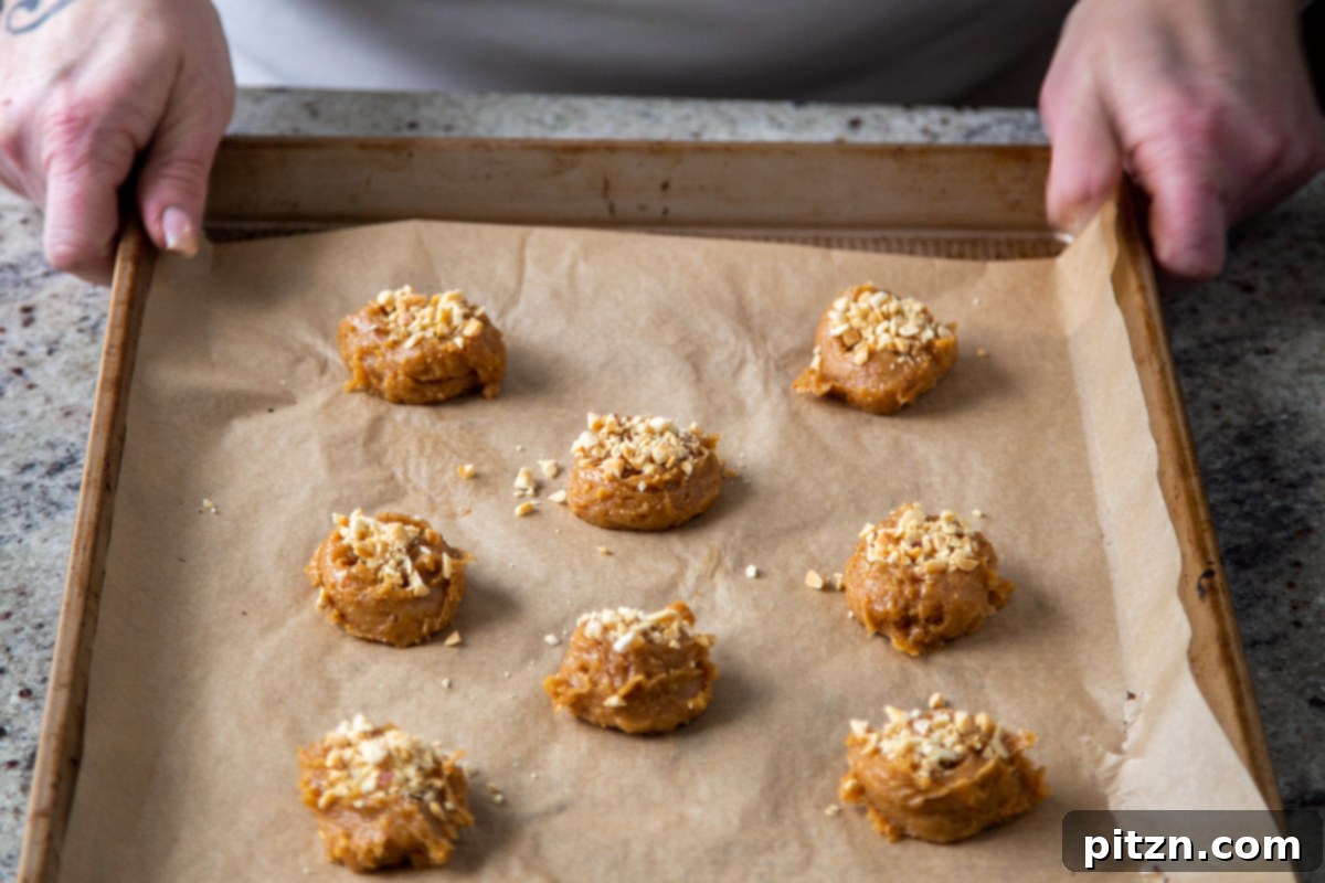 Flourless Peanut Butter Cookies 10 Close-up shot of crushed peanuts being sprinkled onto vegan peanut butter cookie dough balls arranged on a baking sheet, ready for baking.