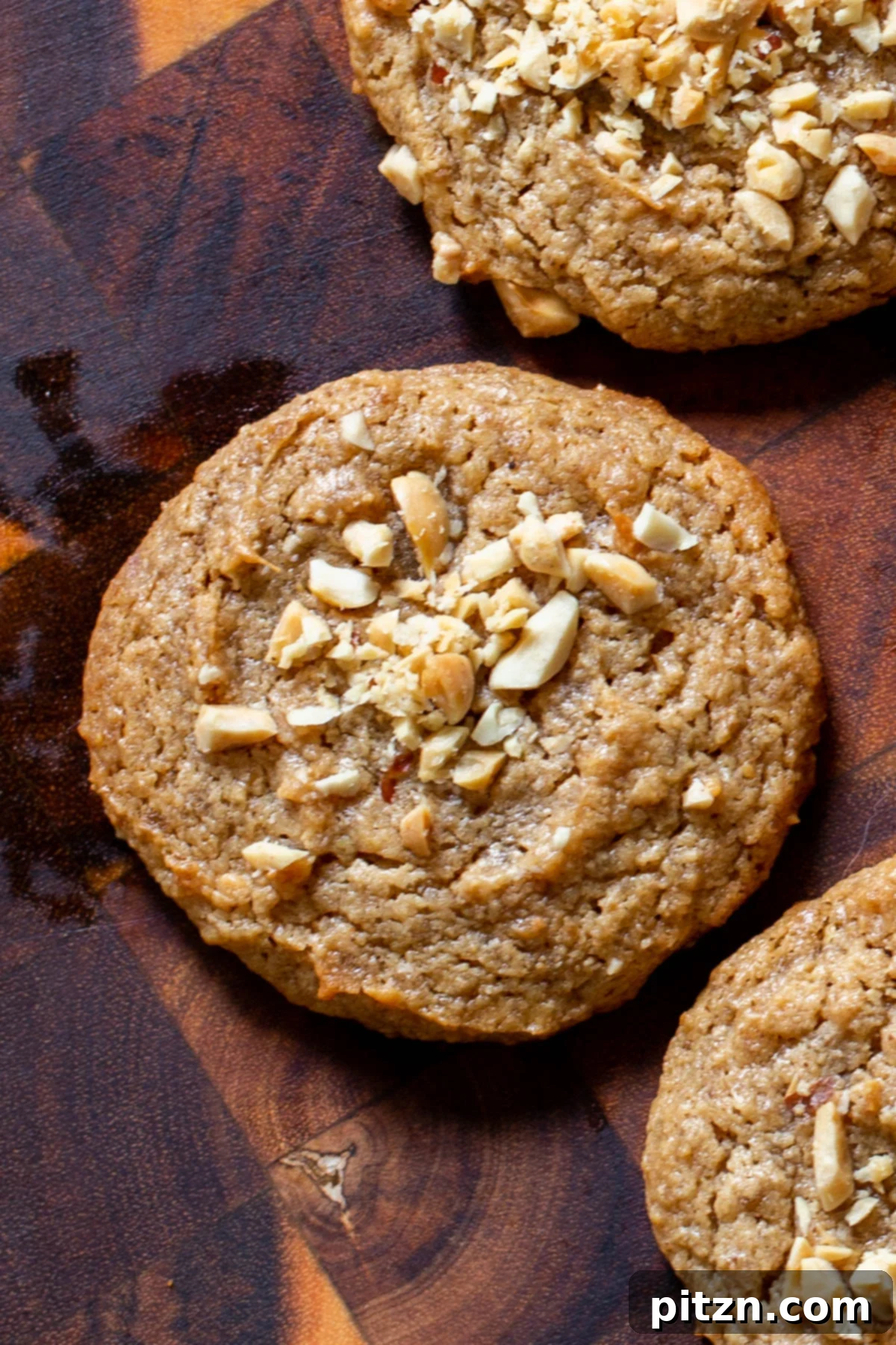 Flourless Peanut Butter Cookies 3 Three perfectly baked vegan no-flour peanut butter cookies arranged on a rustic wooden board, each topped with a delicate scattering of crushed peanuts, highlighting their delightful texture.