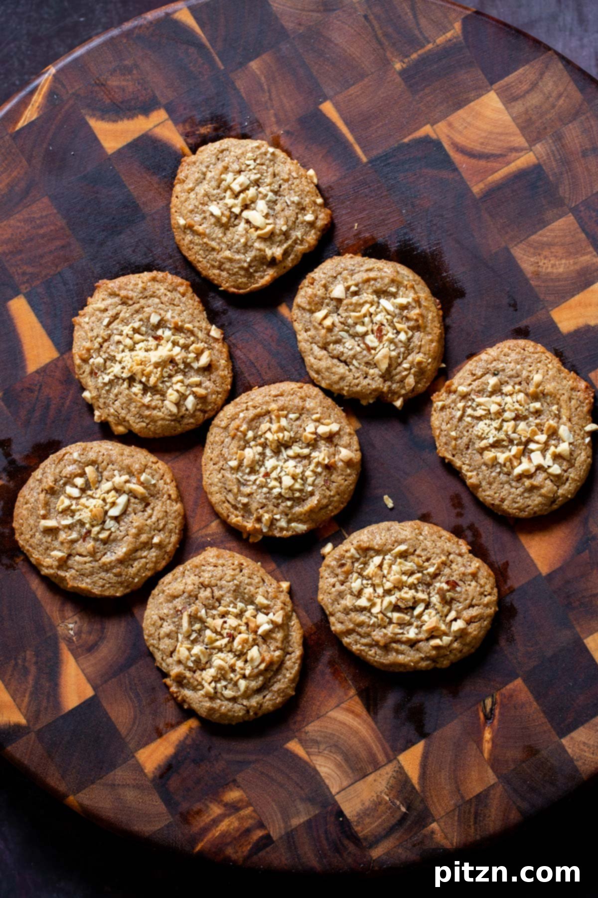 Flourless Peanut Butter Cookies 5 Close-up of a single vegan no-flour peanut butter cookie on a wooden board, showcasing its perfectly baked texture and the rustic charm of crushed peanuts on top.