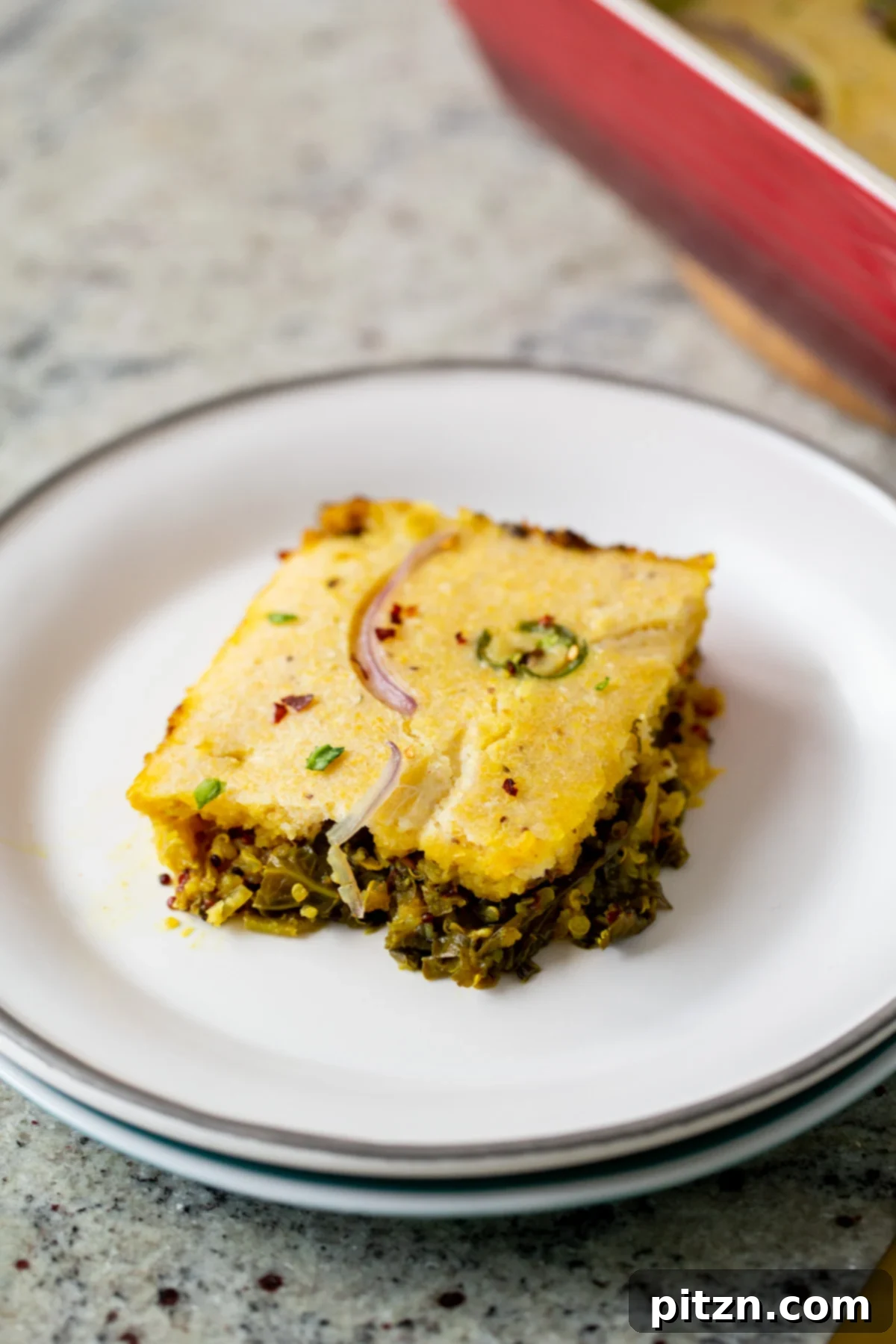 A golden-brown slice of Saag Cornbread Casserole on a white plate, showcasing the vibrant green saag beneath the crusty cornbread topping.