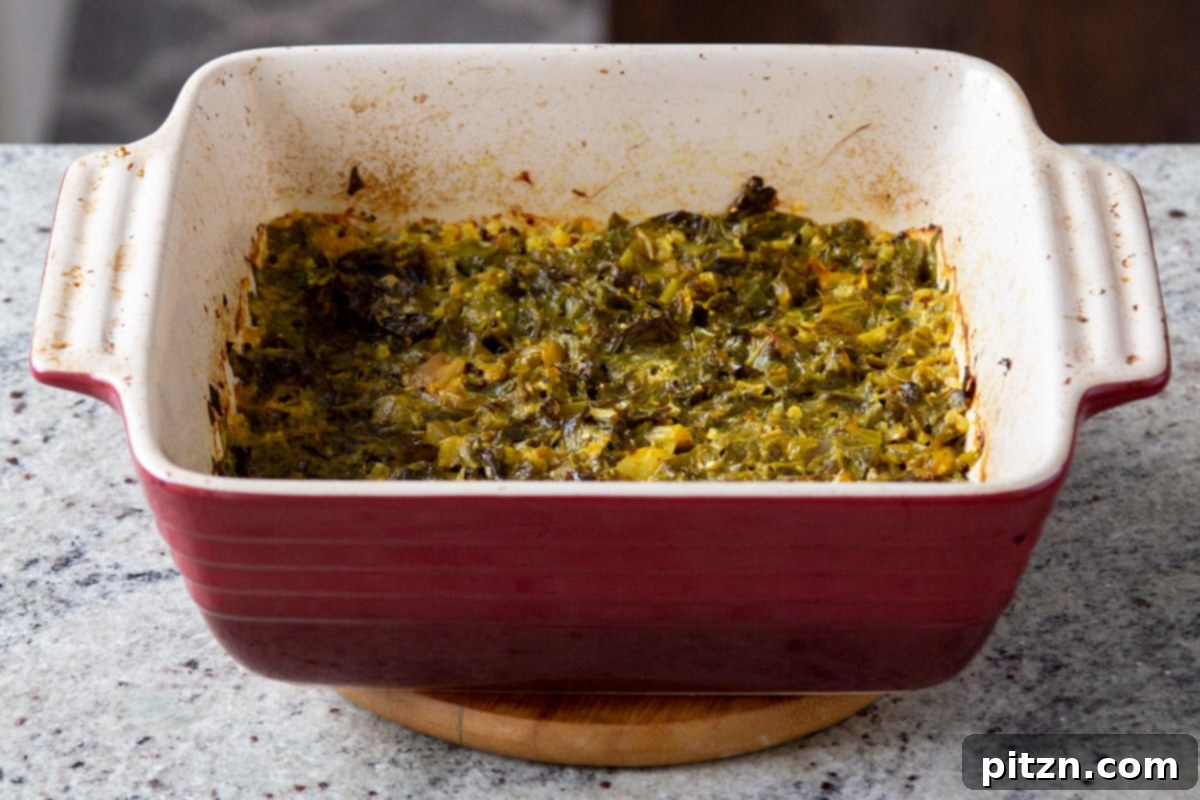 Cooked mustard greens and quinoa in a red casserole dish, fresh from the oven, ready for the next steps of the recipe.