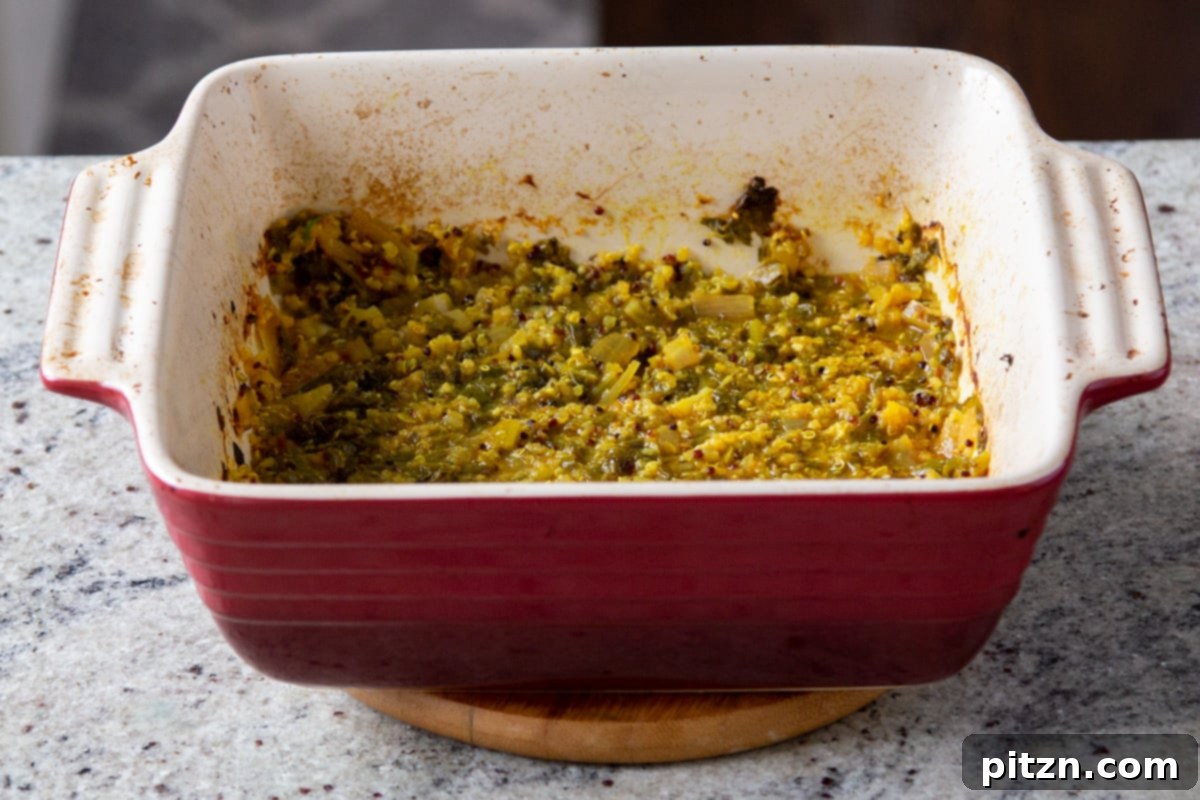 Baked Indian saag stew, rich with mustard greens and quinoa, simmering in a vibrant red casserole dish after its initial bake.