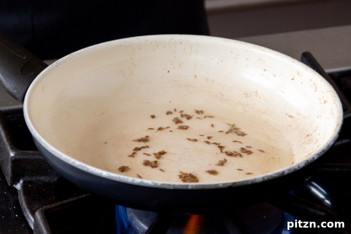 Cumin seeds sizzling in hot oil in a small frying pan, initiating the tempering process for the saag casserole.