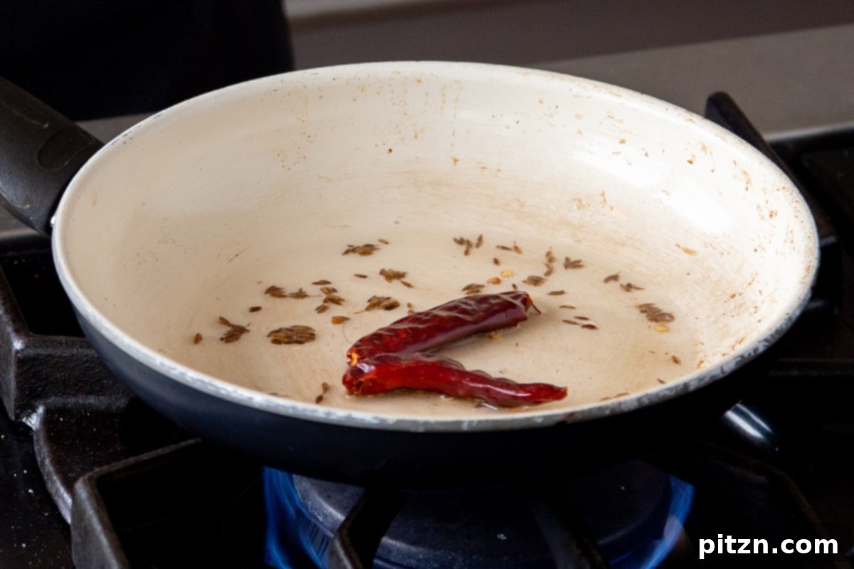 Cumin seeds and dried red chilies frying in oil in a small pan, creating an aromatic tempering for the saag.