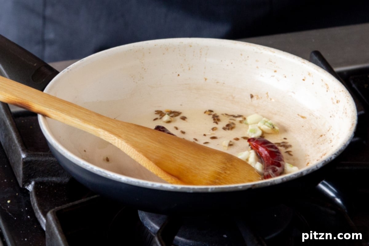 Cumin seeds, minced garlic, and dried red chilies cooking in a frying pan, forming the aromatic tempering for the Saag Cornbread Casserole.