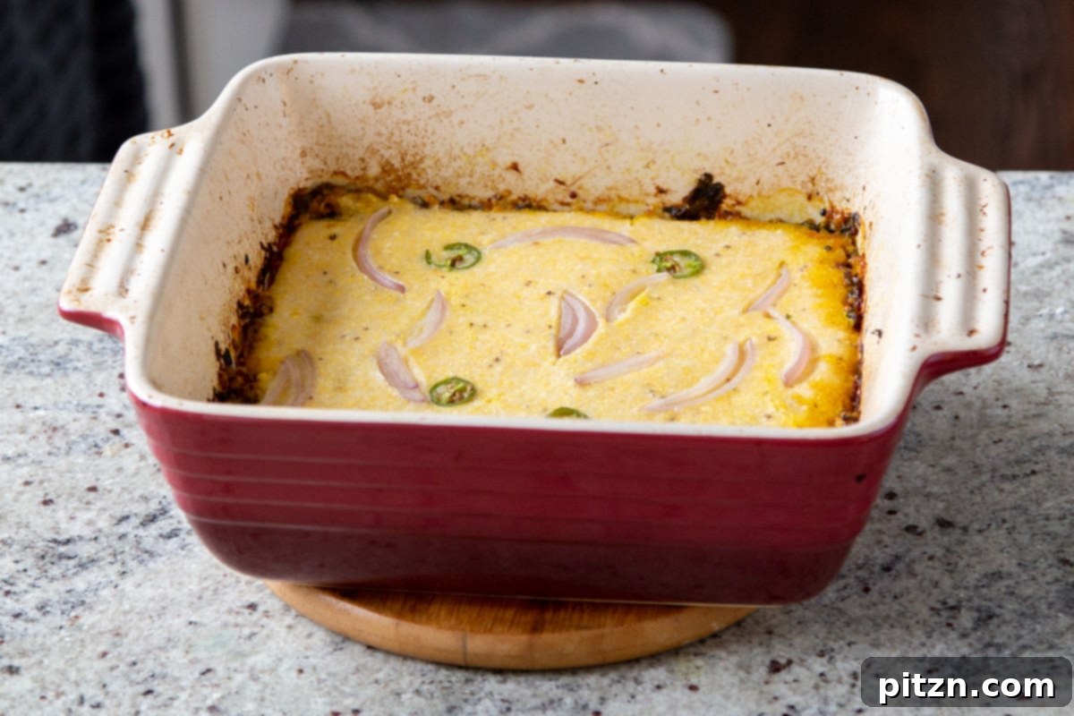 A close-up of the baked cornbread casserole topping, garnished with fresh onion and green chilies, showcasing its golden crust.