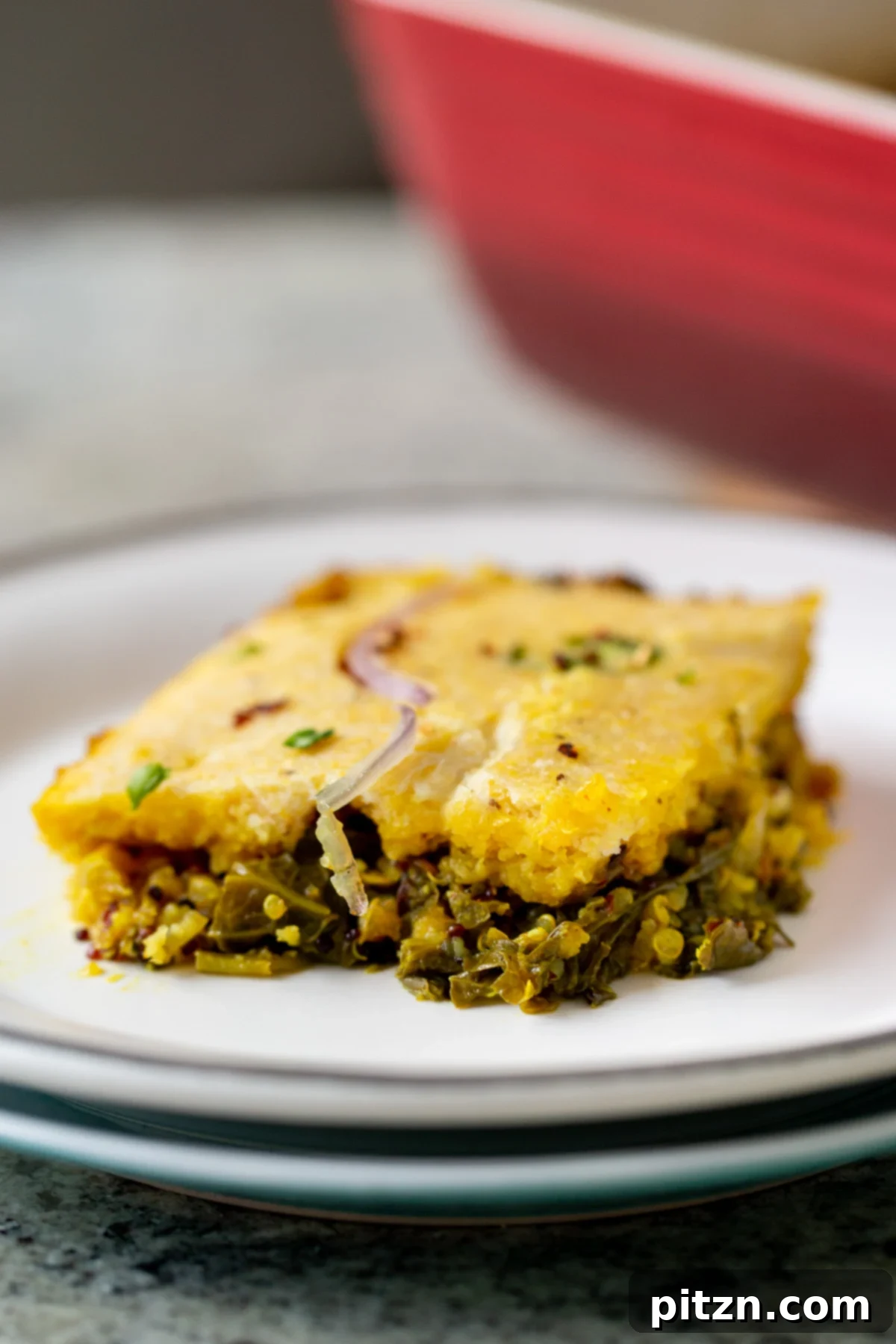 A delectable slice of Saag Cornbread Casserole, featuring the vibrant saag base crowned with golden cornbread, elegantly presented on two stacked white plates.