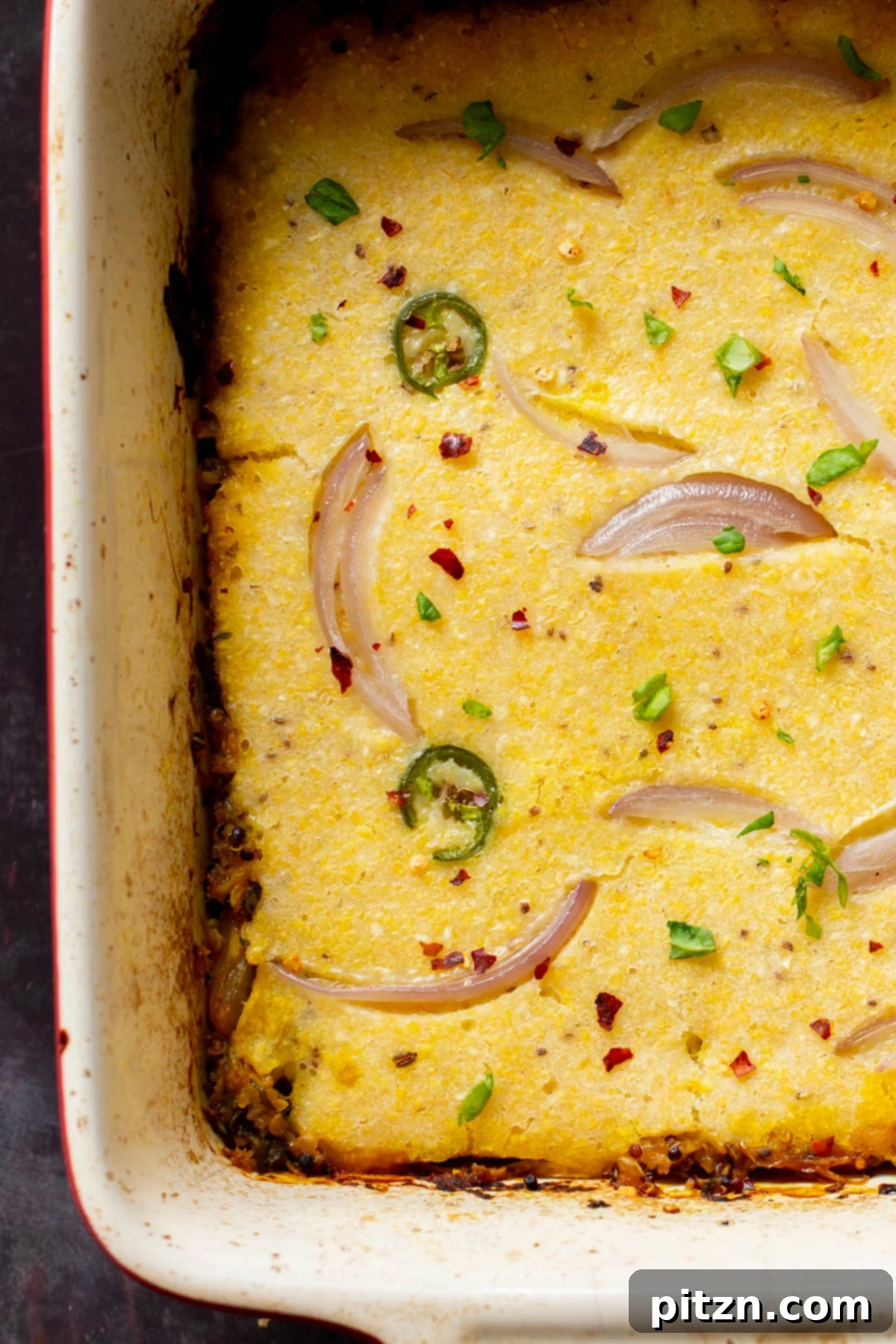 A close-up, inviting overhead view of the vegan Saag Cornbread Casserole, highlighting the textures of the golden cornbread and the rich, spiced saag.