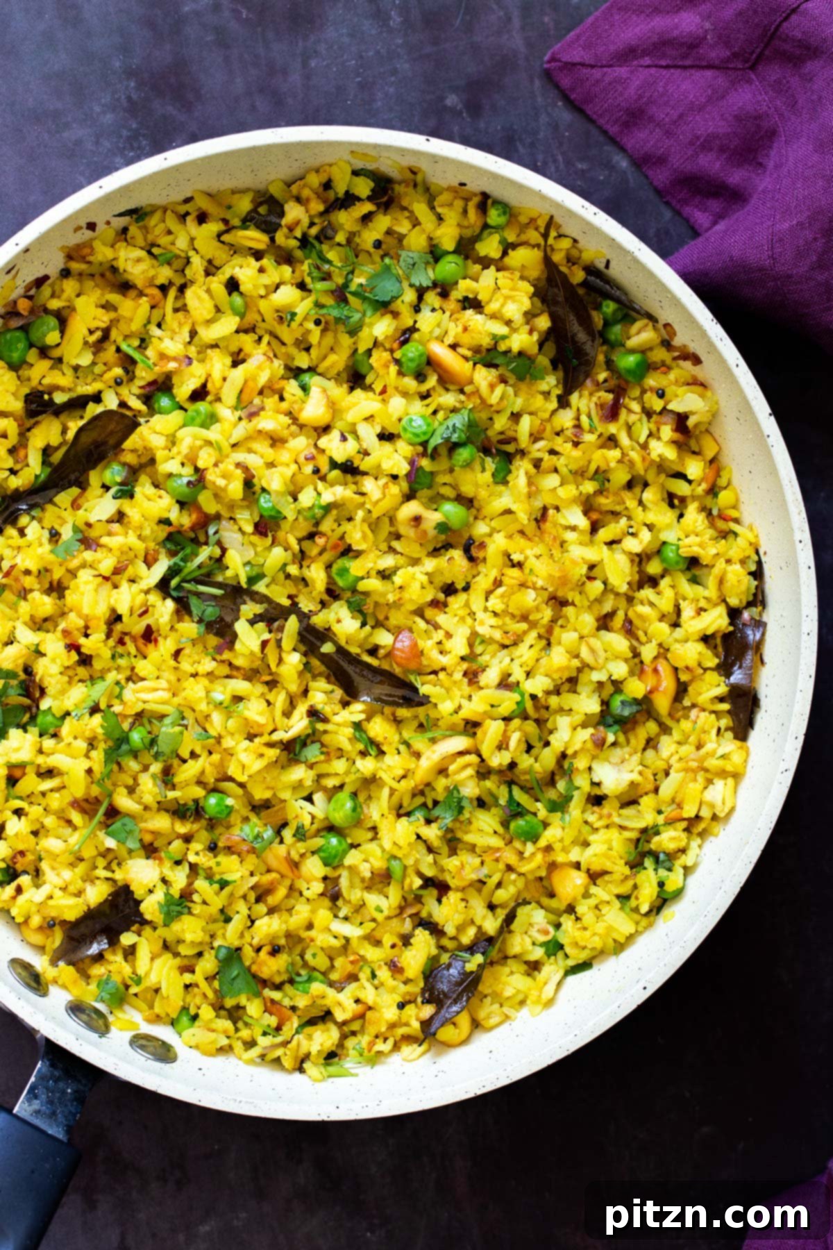 Spiced Onion Poha: Savory Flattened Rice Breakfast 2 A sauteeing pan filled with Indian Kanda Poha, featuring fluffy rice flakes, green peas, and vibrant spices, garnished with fresh cilantro.
