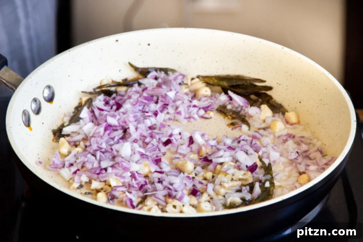 Spiced Onion Poha: Savory Flattened Rice Breakfast 8 Diced red onion and tempered spices, including mustard seeds and curry leaves, sautéing in a frying pan until the onion is translucent.