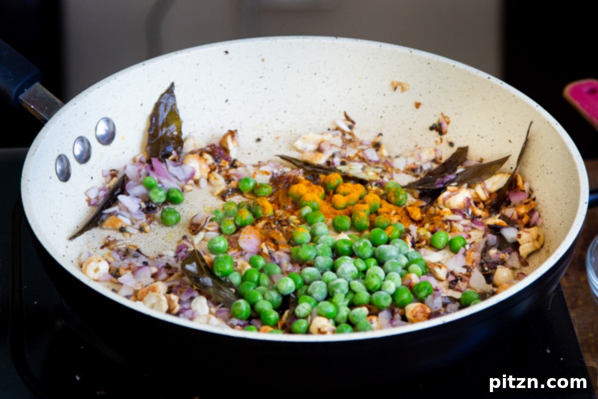 Spiced Onion Poha: Savory Flattened Rice Breakfast 9 Green peas, turmeric, and cayenne pepper being added to the sautéed onions and spices in a frying pan, ready to be mixed.