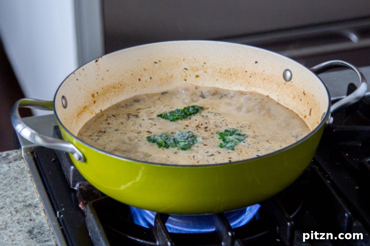 Fresh spinach leaves being stirred into a creamy vegan Zuppa Toscana soup in a saucepan.