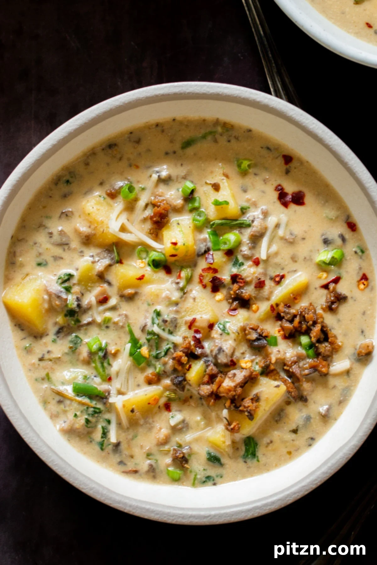 Overhead shot of a bowl of creamy vegan Zuppa Toscana, topped with fresh chopped chives, on a rustic background.