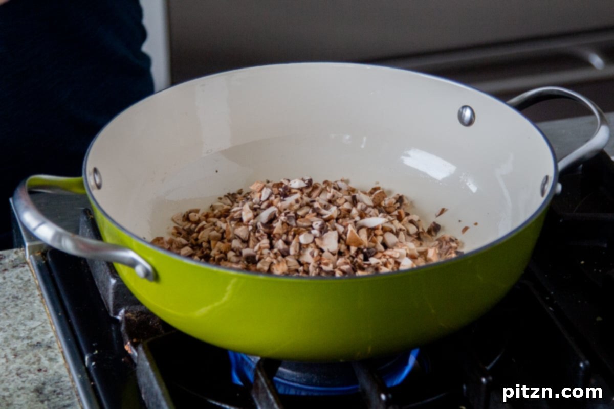 Chopped mushrooms sautéing in a large saucepan with a small amount of oil.