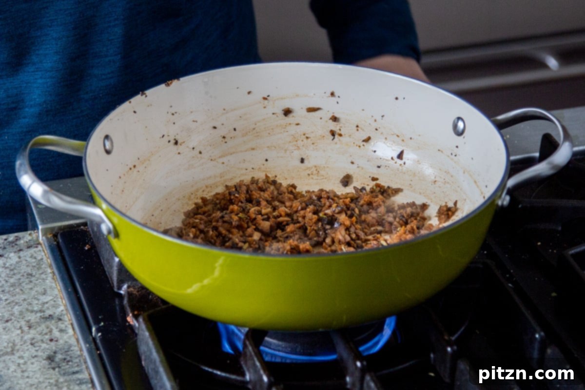 Vegan sausage crumbles frying in a pan with sautéed mushrooms.