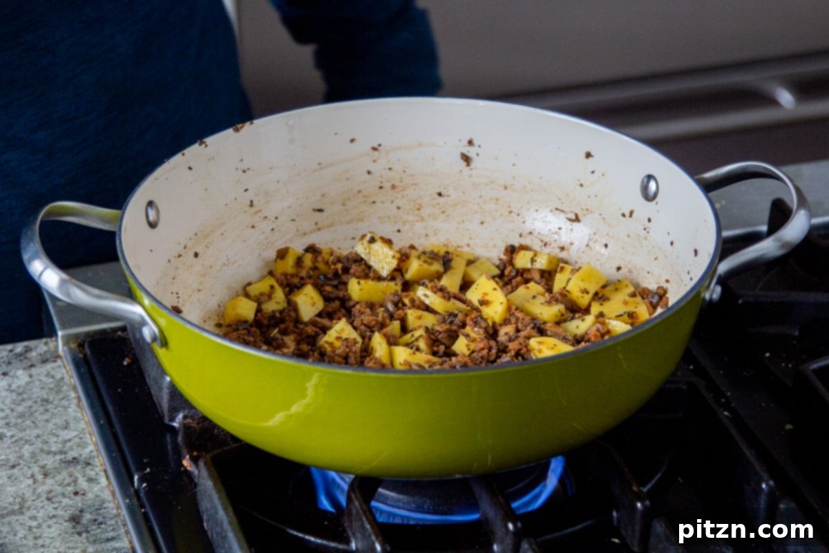 A saucepan filled with vegan sausage crumbles, cubed potatoes, and broth, simmering gently.