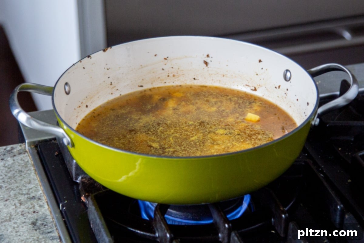Cubed potatoes and vegan sausage crumbles simmering in a rich broth in a green saucepan.