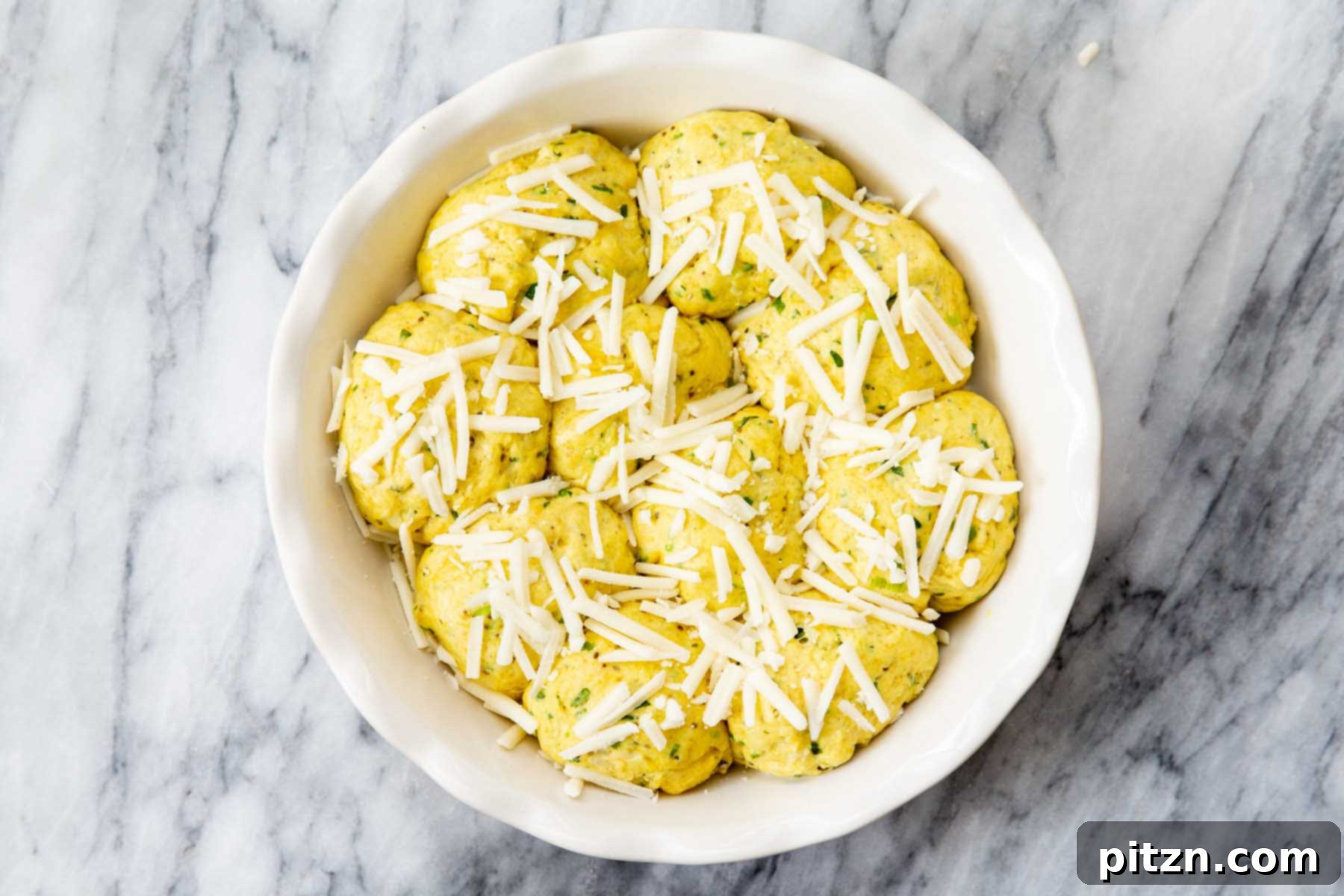 Golden Mustard Coconut Rolls 17 Dough balls arranged in a baking dish with vegan cheese generously sprinkled on top, ready for baking.