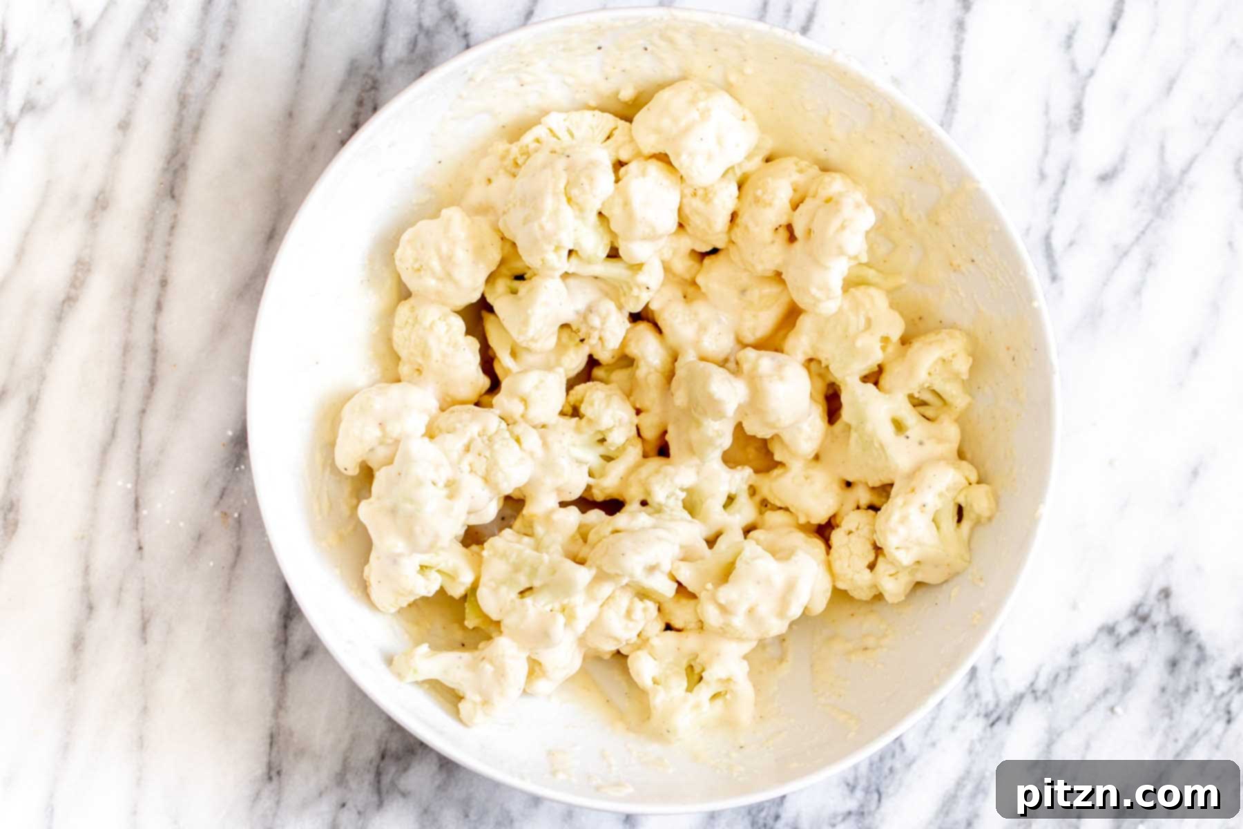 Cauliflower florets fully coated in a light, even batter after tossing, prepared for baking.